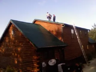 Crew on the ridge of a green metal roof on a two story log home in Adams