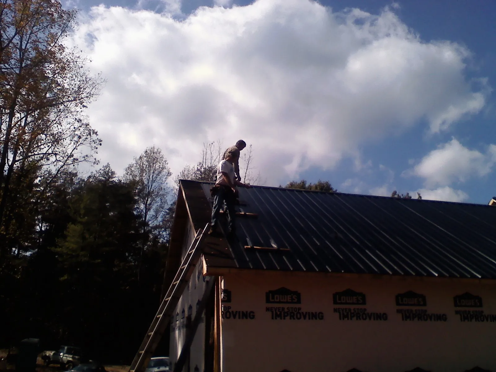Roofer fastening dark metal panels high against a cloudy sky, from a Roof Inspection job in Adams
